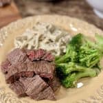 This is a picture of a yellow plate topped with noodles, steamed broccoli and sliced flank steak that has been marinated.
