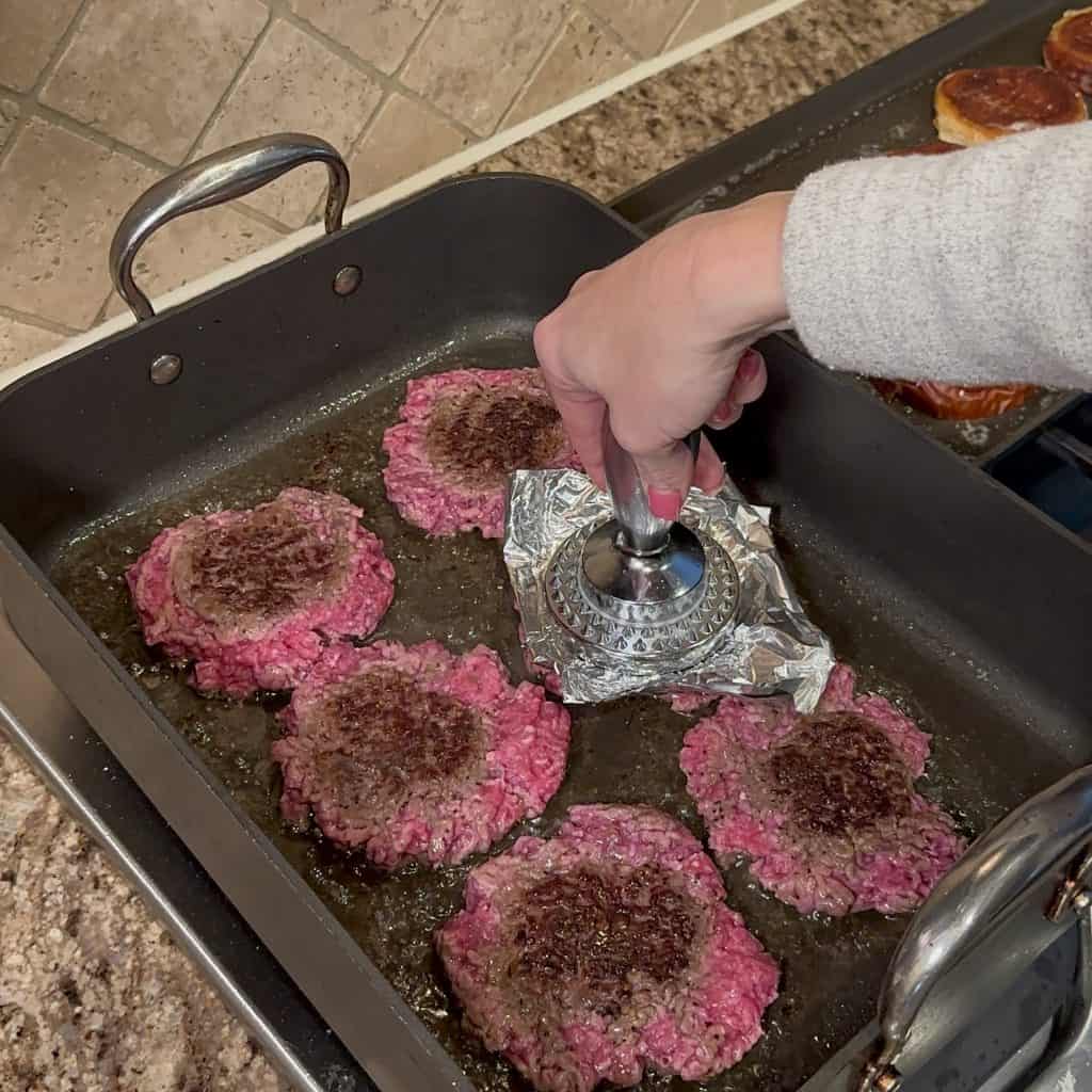 pressing burger patties flat in a pan