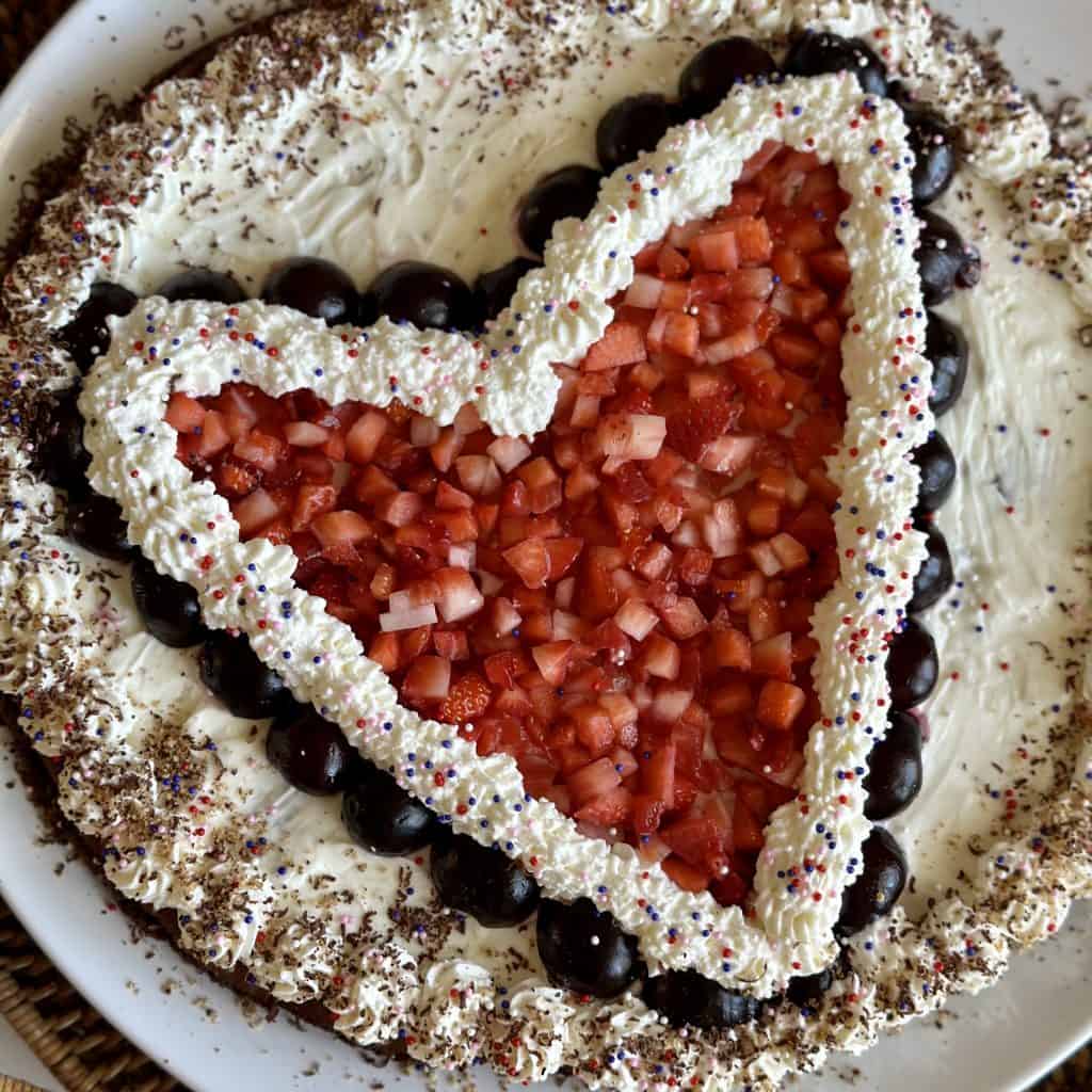 a large round brownie decorated with whipped cream, strawberries and cherries.