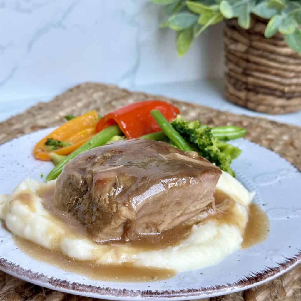 Pork roast with gravy served over mashed potatoes with a side of vegetables
