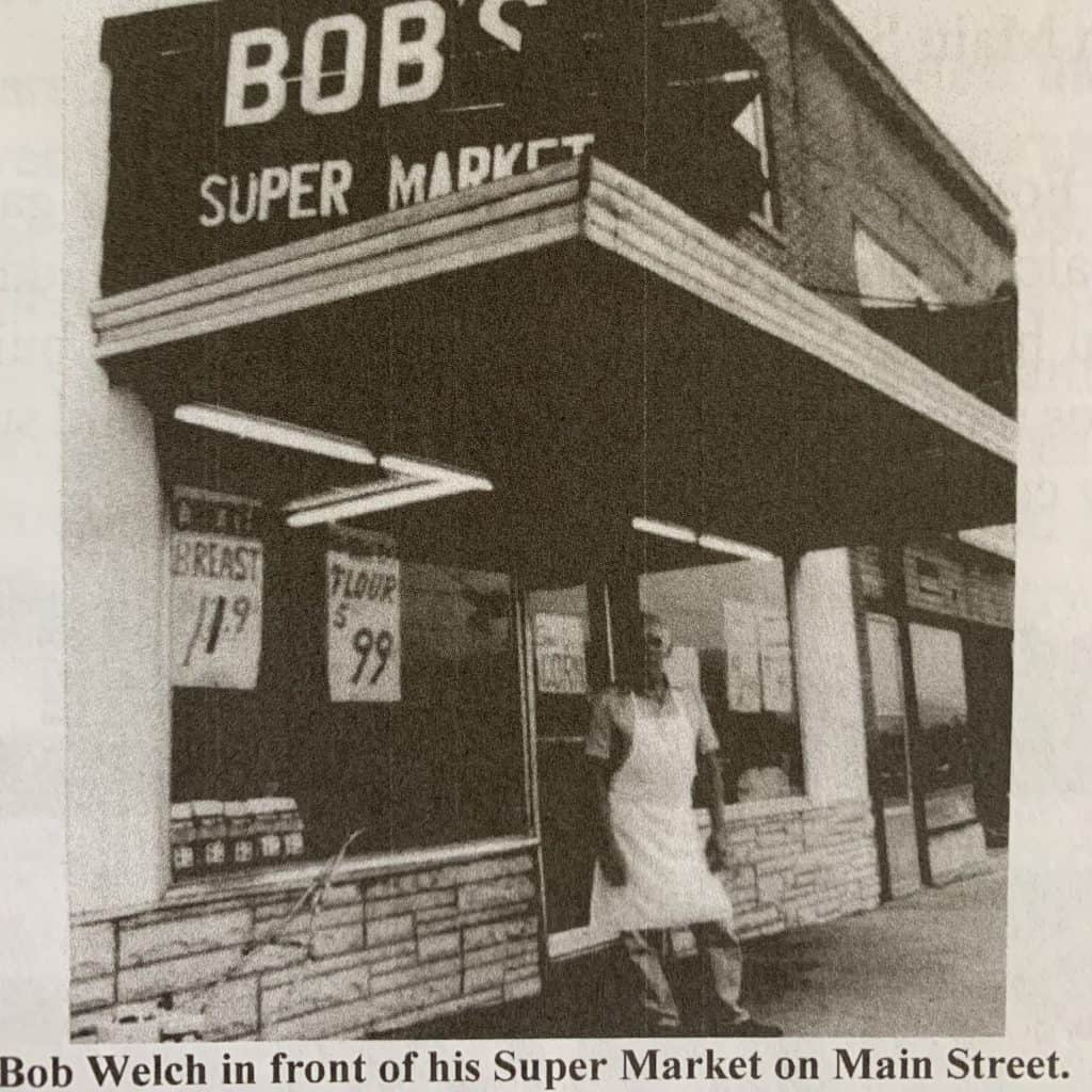 old black and white photo of a man standing in front of grocery store