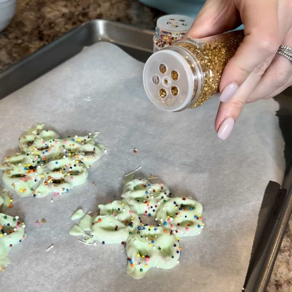 sprinkling sprinkles on coated pretzels
