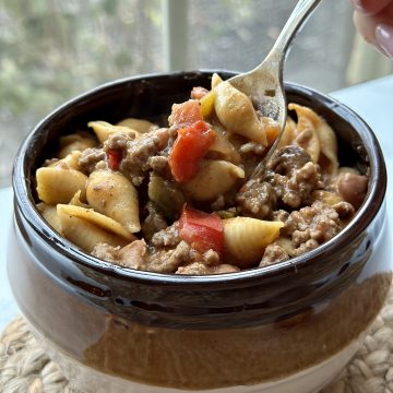 This is a picture of a brown bowl filled with soup. The soup has shell shaped pasta with tomatoes and ground beef.