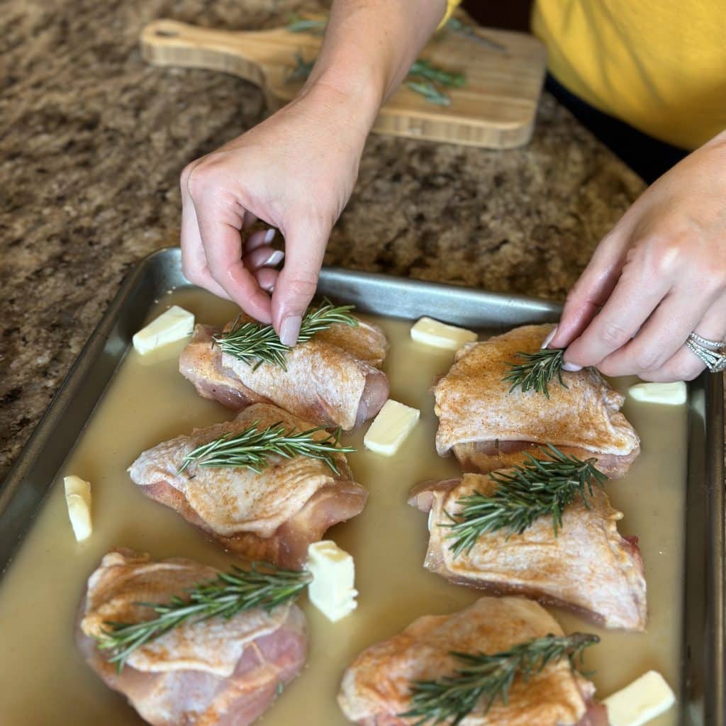 Placing fresh rosemary sprigs on each chicken thigh