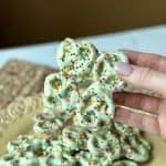 This is a picture of pretzels that have been dipped in green colored vanilla candy coating and they have rainbow sprinkles on top.