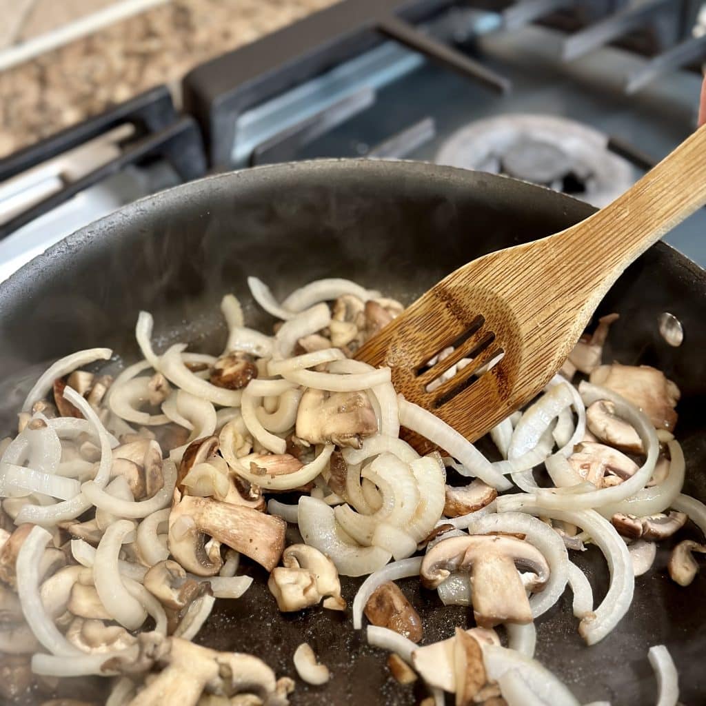 sautéing mushrooms and onions in a pan with a wooden spoon 