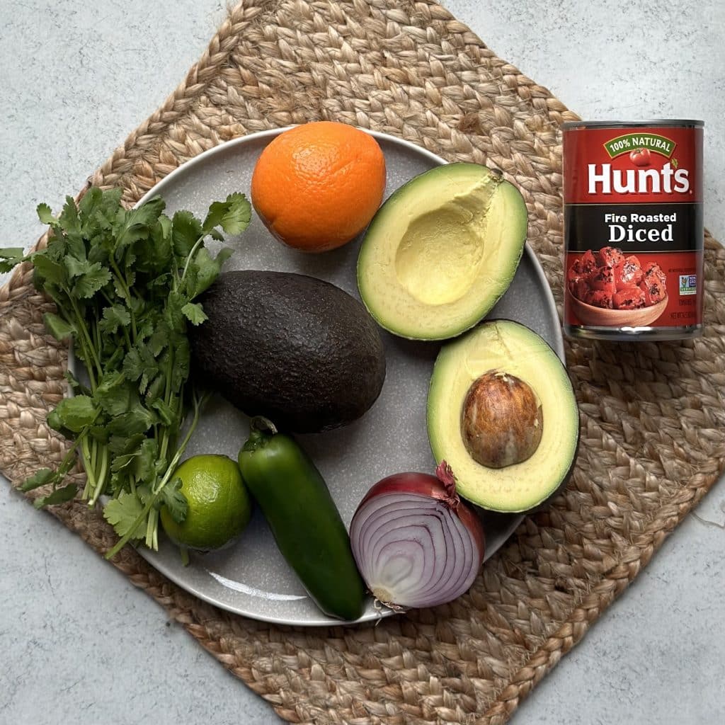 The ingredients to make guacamole: fire roasted diced tomatoes, avocado, red onion, jalapeño, lime, avocado, orange and cilantro