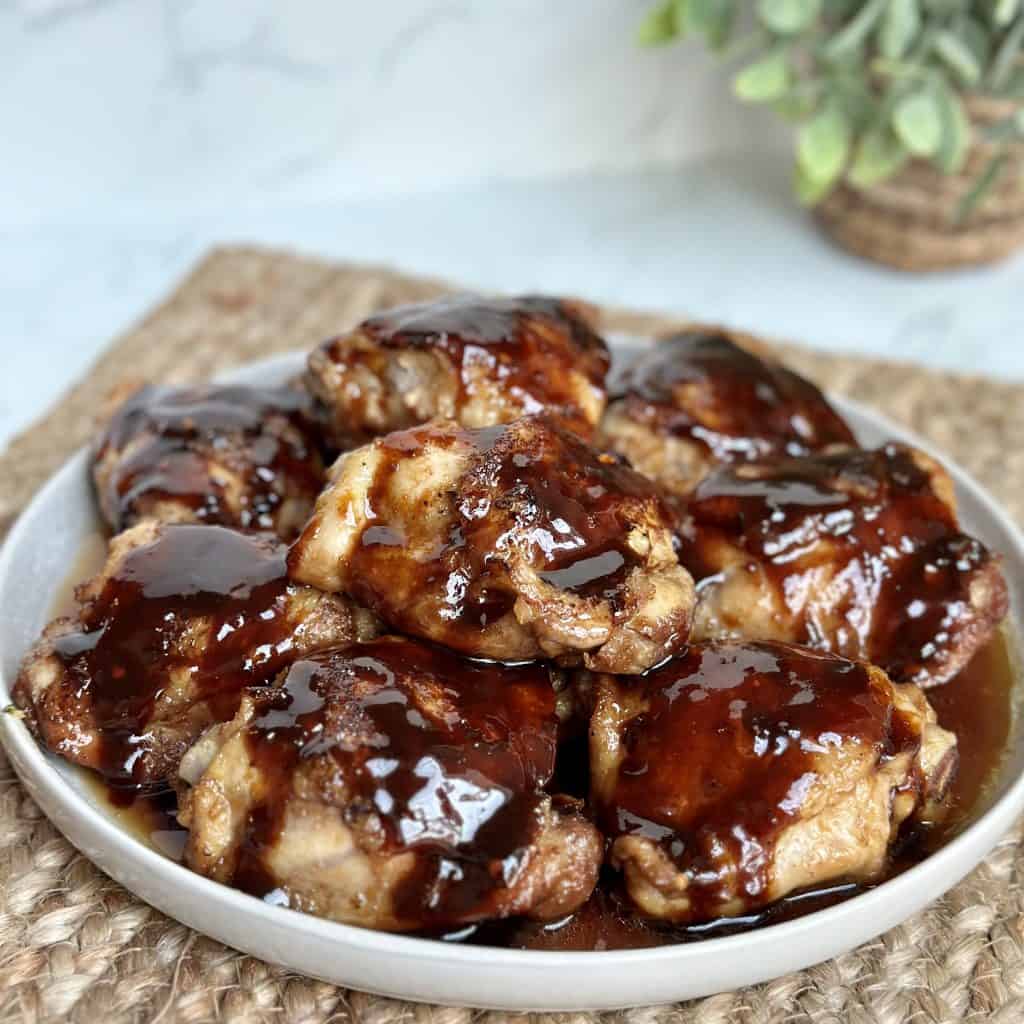 This is a picture of a plate full of 10 glazed chicken thighs. The glaze looks brownish purple. It’s sitting on a brown placemat.