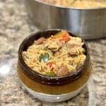 This is a picture of a bowl sitting on the counter filled with a seasoned pasta and rice blend, sliced sausage and cooked red and green peppers and onions.