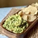 This is a picture of green guacamole and chips. The guacamole has in it some red fire roasted tomatoes and cilantro as well as lime and seasonings.