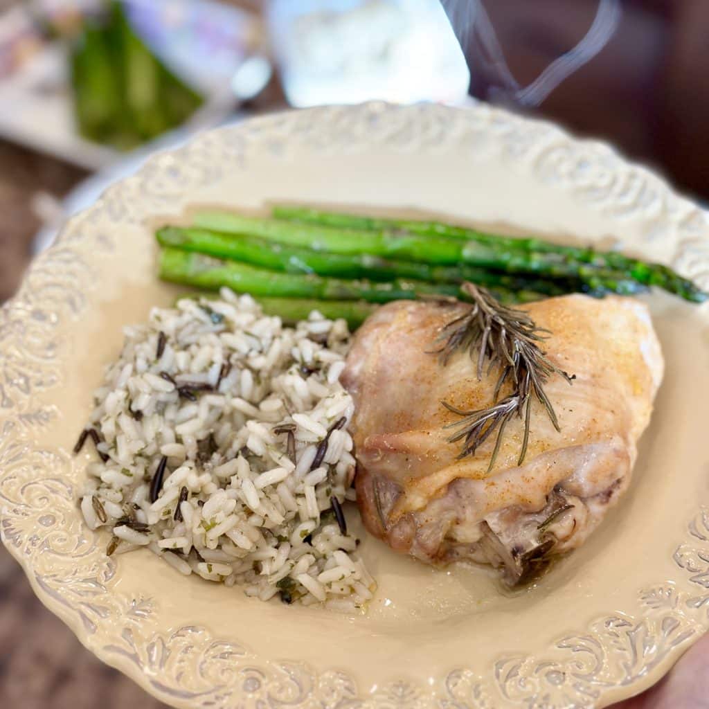 Dinner plate with cooked asparagus spears, wild rice, baked chicken and rosemary.