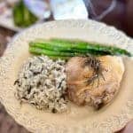 This is a picture a dinner plate filled with cooked asparagus spears, wild rice and a baked chicken thigh with rosemary on top.