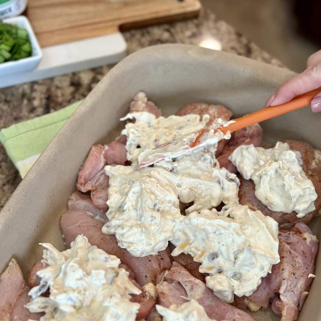 Spreading creamy cheesy bacon mixture on top of chicken thighs