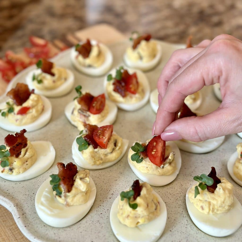 Placing a tomato quarter garnish on Deluxe BLT Deviled Eggs  displayed on a serving tray