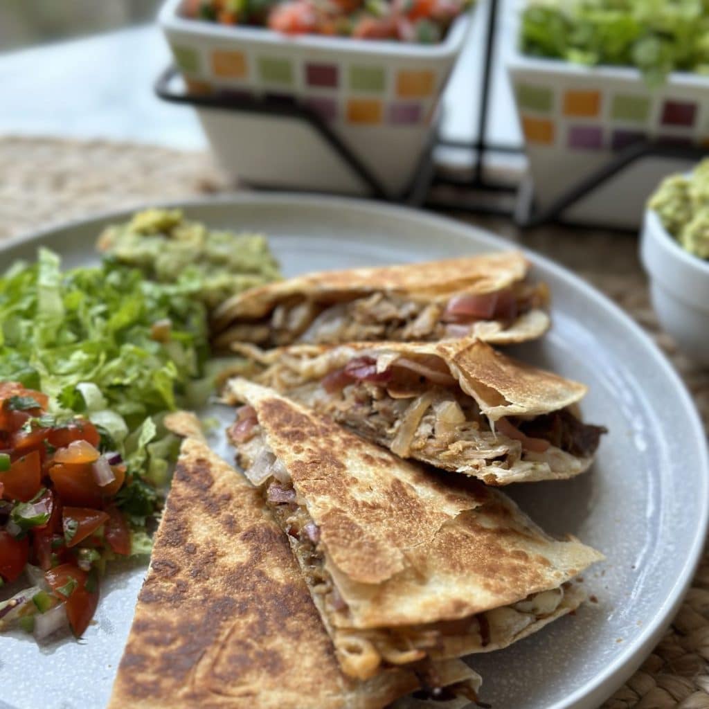 A plate topped with a shredded pork quesadilla, shredded lettuce and pico de gallo.