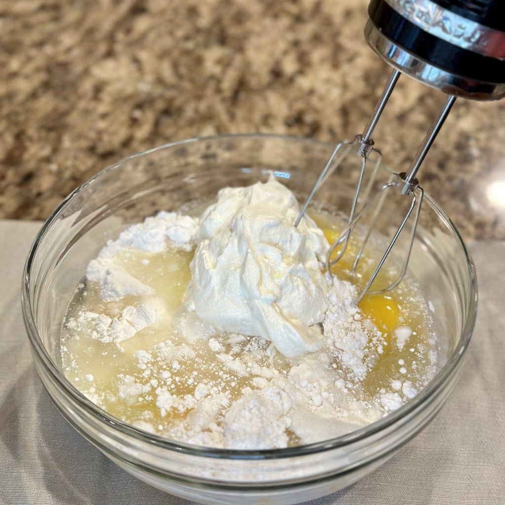 A hand mixer and mixing bowl filled with cake mix and ingredients to make a cake