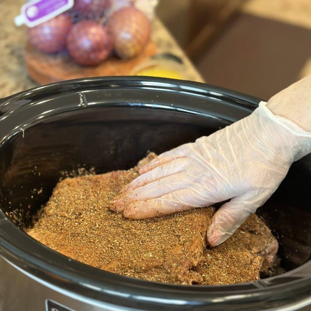 Patting dry seasoning and zest on a pork shoulder in a crockpot.