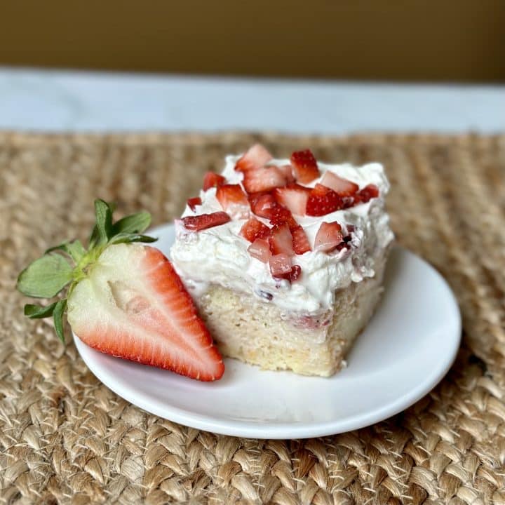 A slice of vanilla cake with whipped cream on top and chopped strawberries with a strawberry half on the side