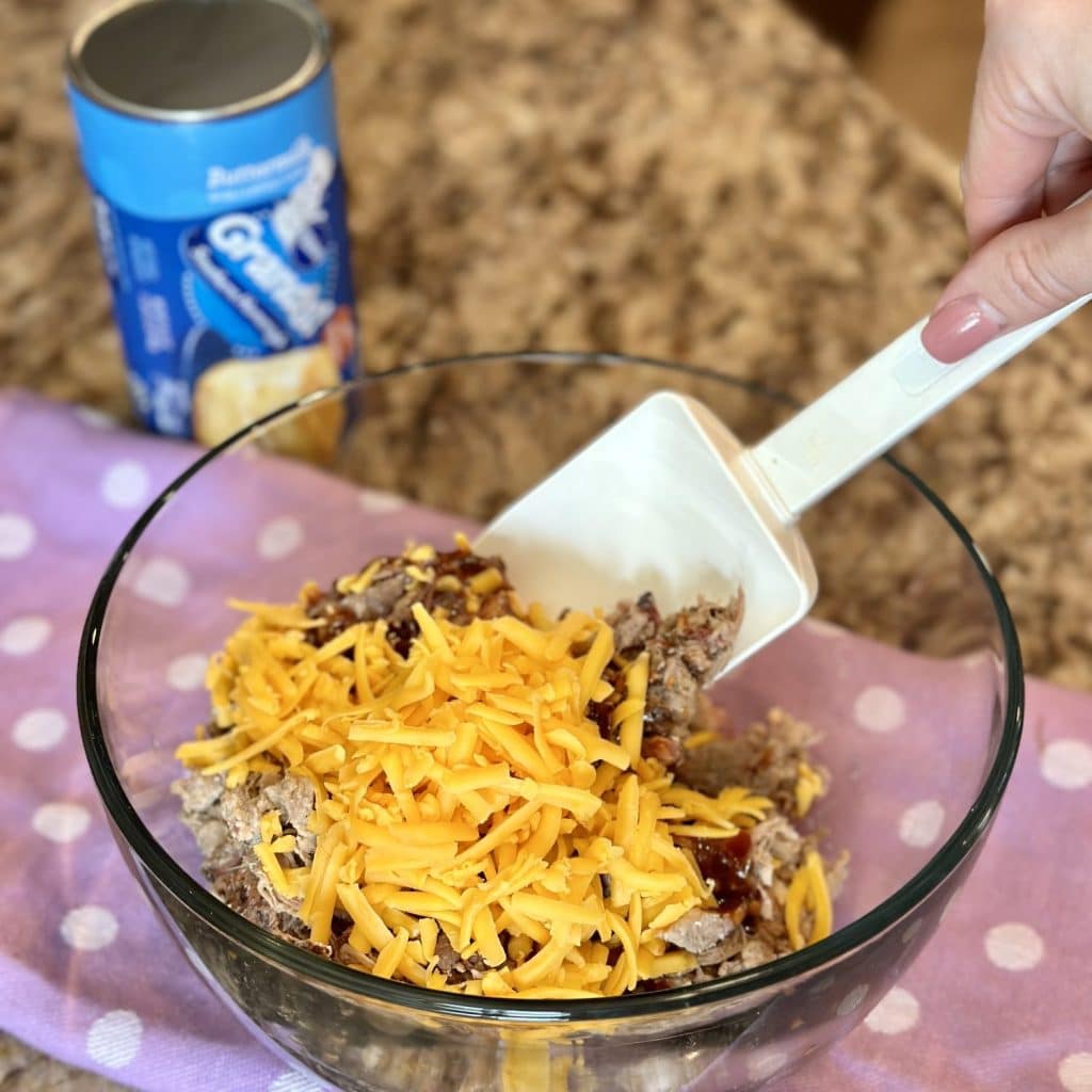 A bowl with cooked pulled pork, cheddar cheese and barbecue sauce ready to mix together.
