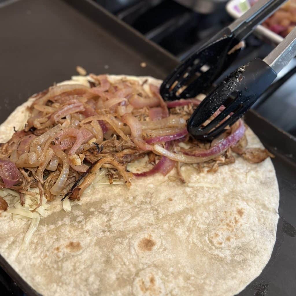 using tongs to fill a tortilla with carnitas