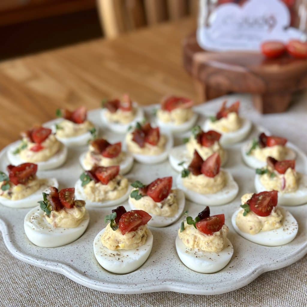Deluxe BLT Deviled Eggs garnished with cherry tomato wedges, greens and bacon crumbles on a serving tray