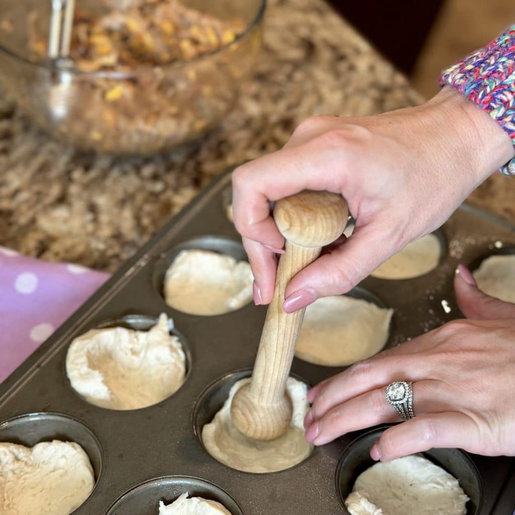 Refrigerated biscuit dough being pressed into a muffin pan