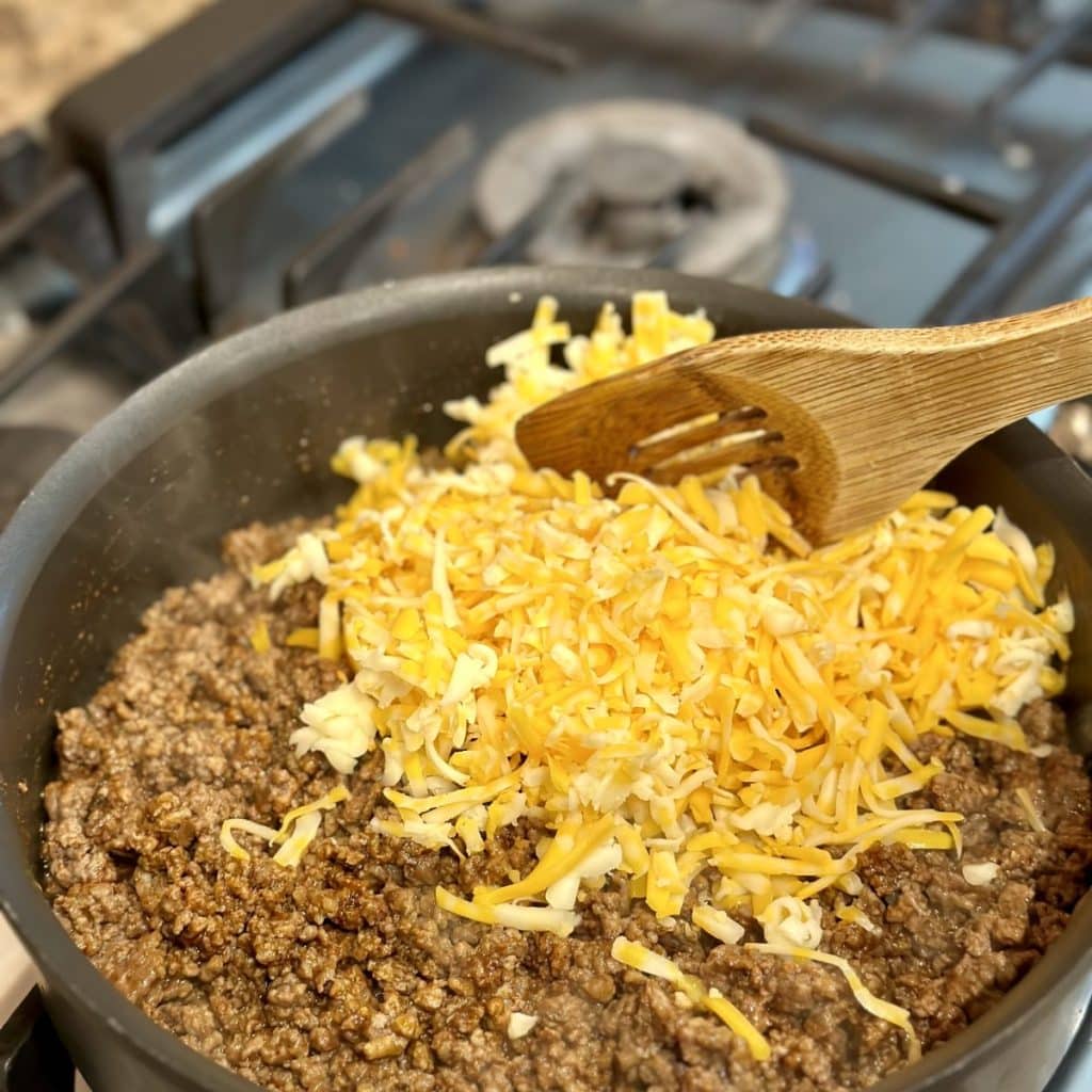 Ground beef and shredded cheese being mixed into a skillet