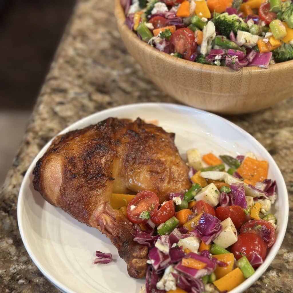 A dinner plate with a roasted chicken quarter and a serving of a vegetable salad blend