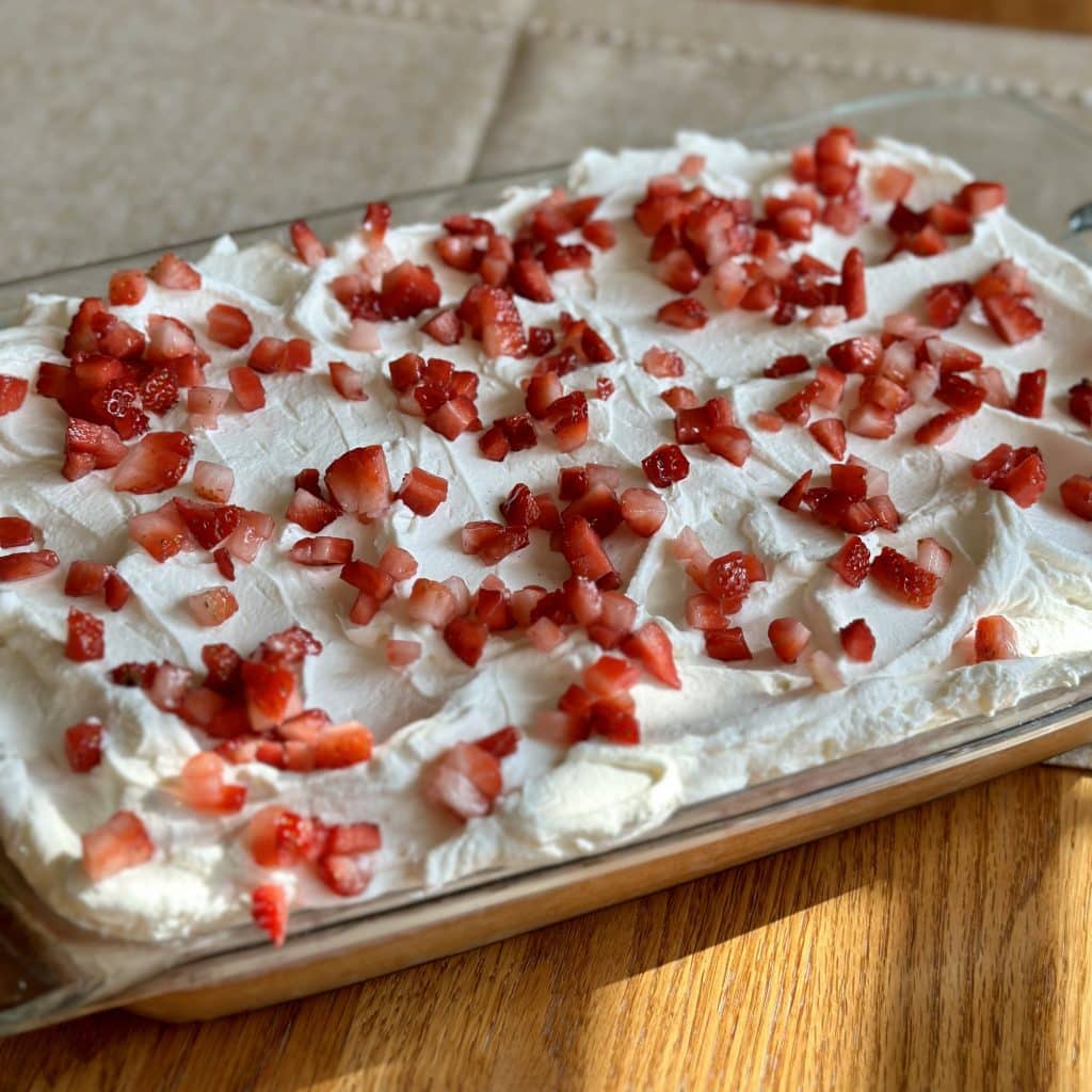 A vanilla cake topped with whipped topping and chopped strawberries