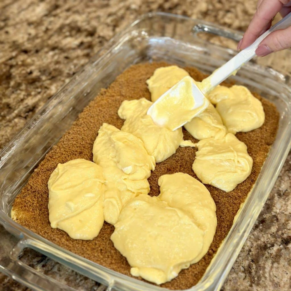 Cake batter in a glass dish. First layer is half the batter, then a layer of brown sugar cinnamon, then the remaining batter.