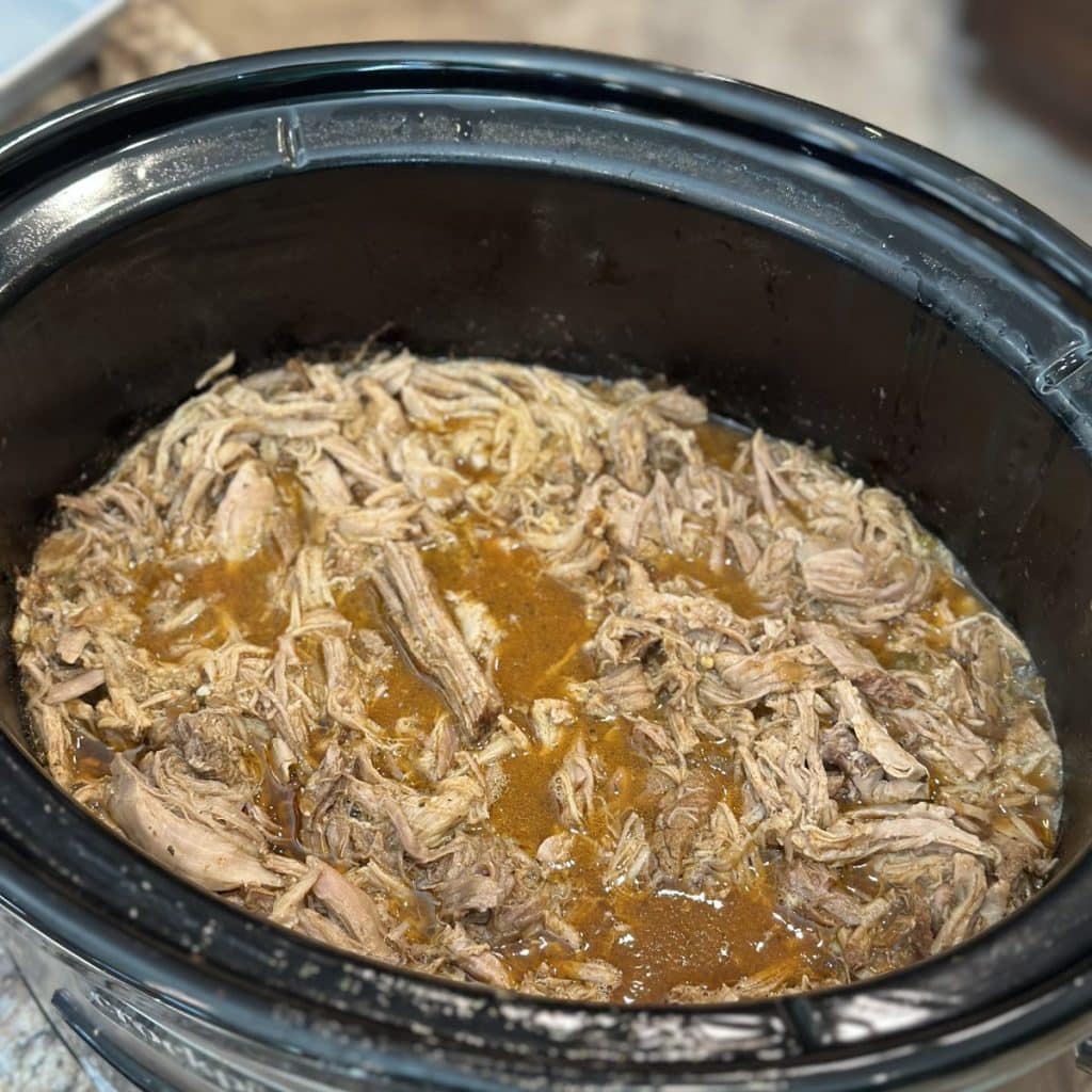 A shredded up pork shoulder in juices in a crockpot.