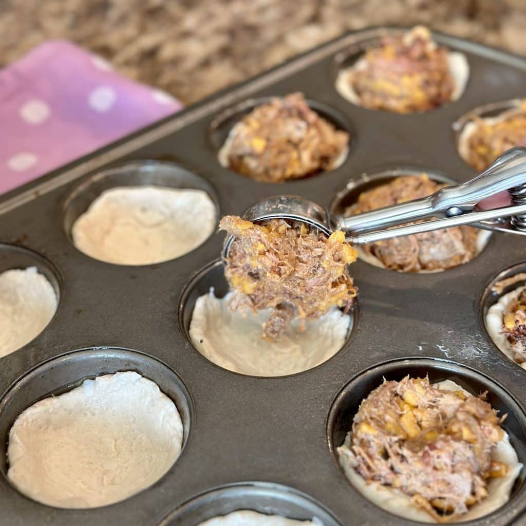 Barbecue filling scooped into biscuit dough in a muffin pan