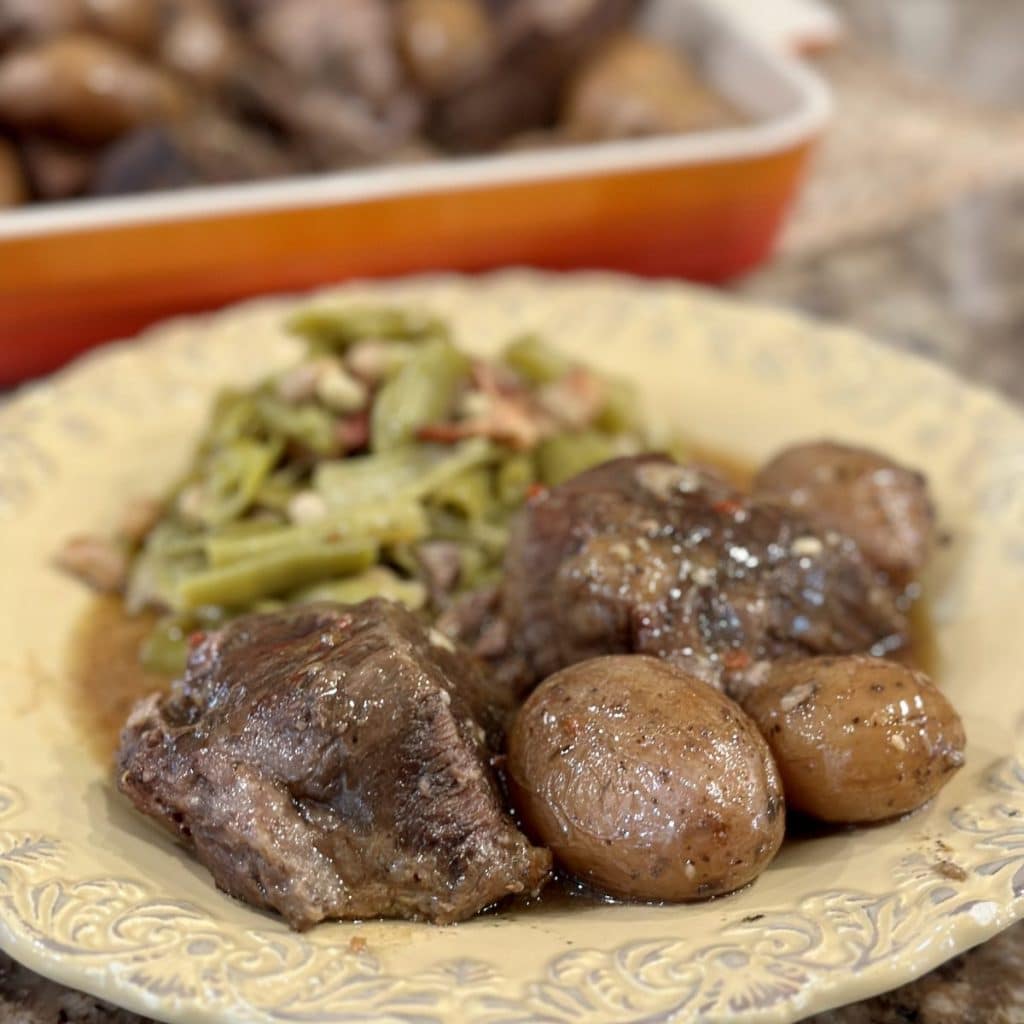 A plate of roast beef, potatoes, brown gravy and green beans