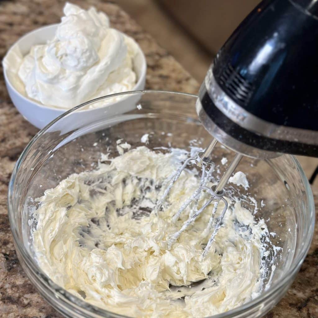 Cream cheese being whipped with a hand mixer in a bowl.