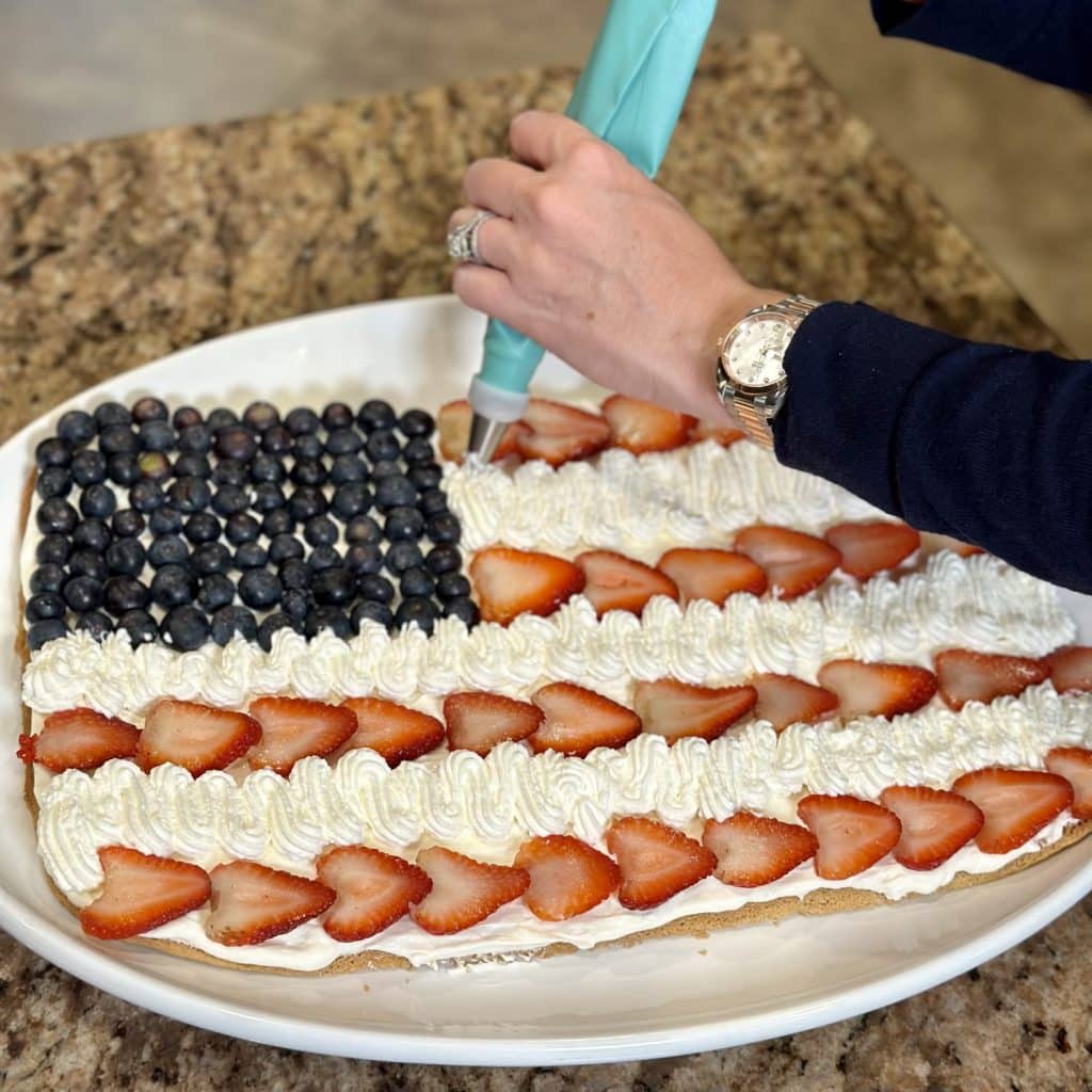 Decorating a sugar cookie like an American flag with strawberries, blueberries and whipped cream cheese frosting