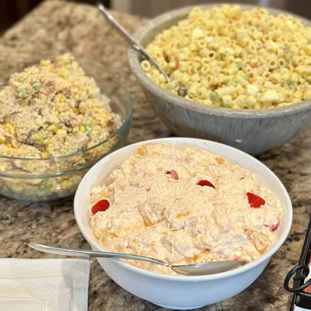 3 salads on a counter: orange jello salad, macaroni salad and cornbread chicken salad.