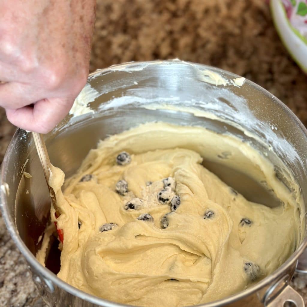 Folding blueberries into cake batter in a mixing bowl.