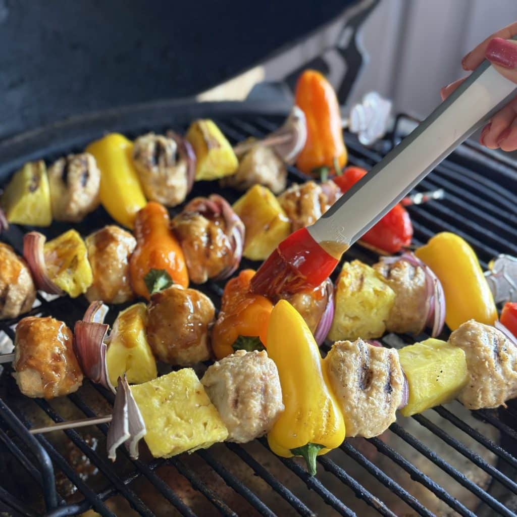 Basting meatball skewers on a grill with a glaze