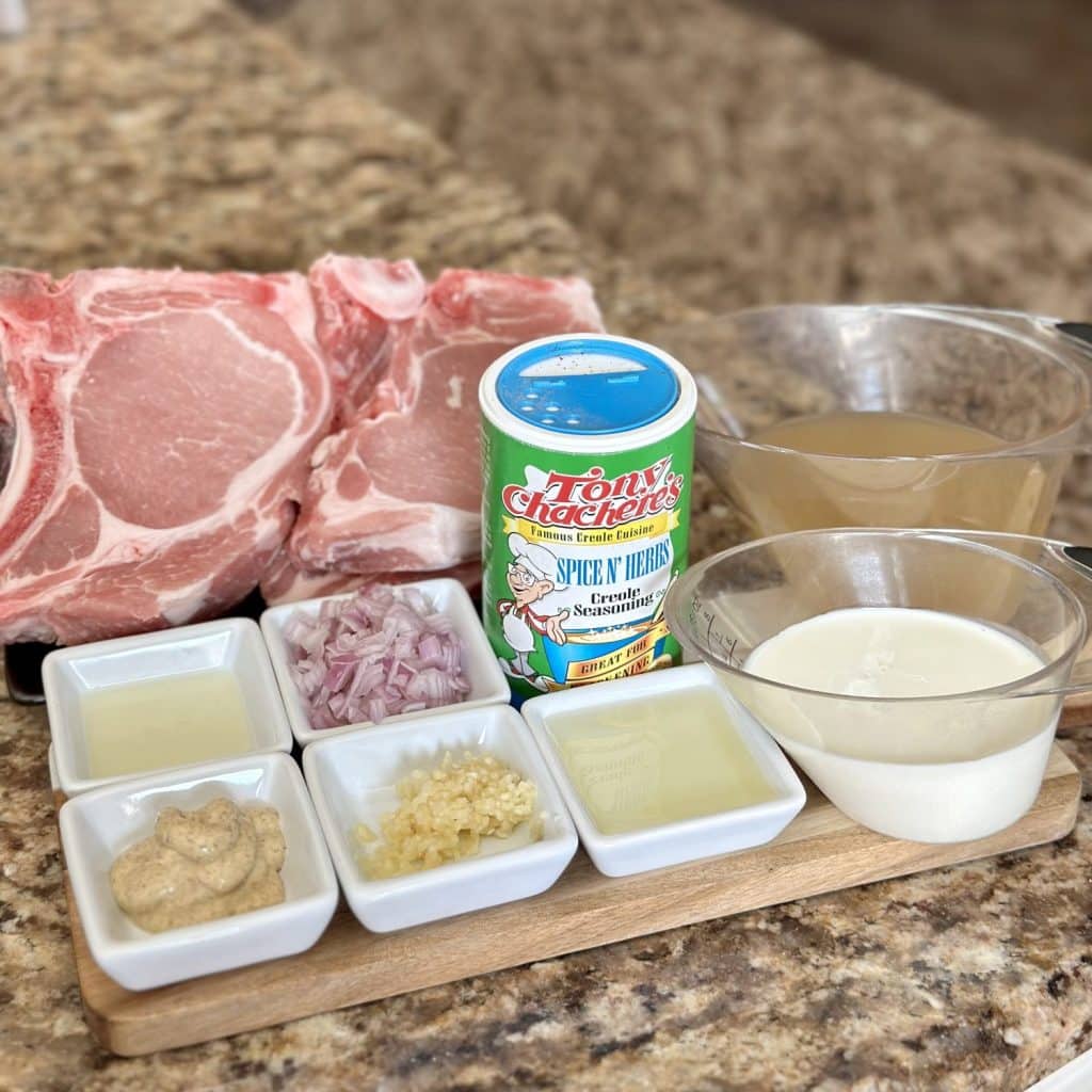 Ingredients to make thick and juicy pork chops including garlic, shallot, lemon juice, dijon mustard, cajun seasoning, broth, cream and pork chops.