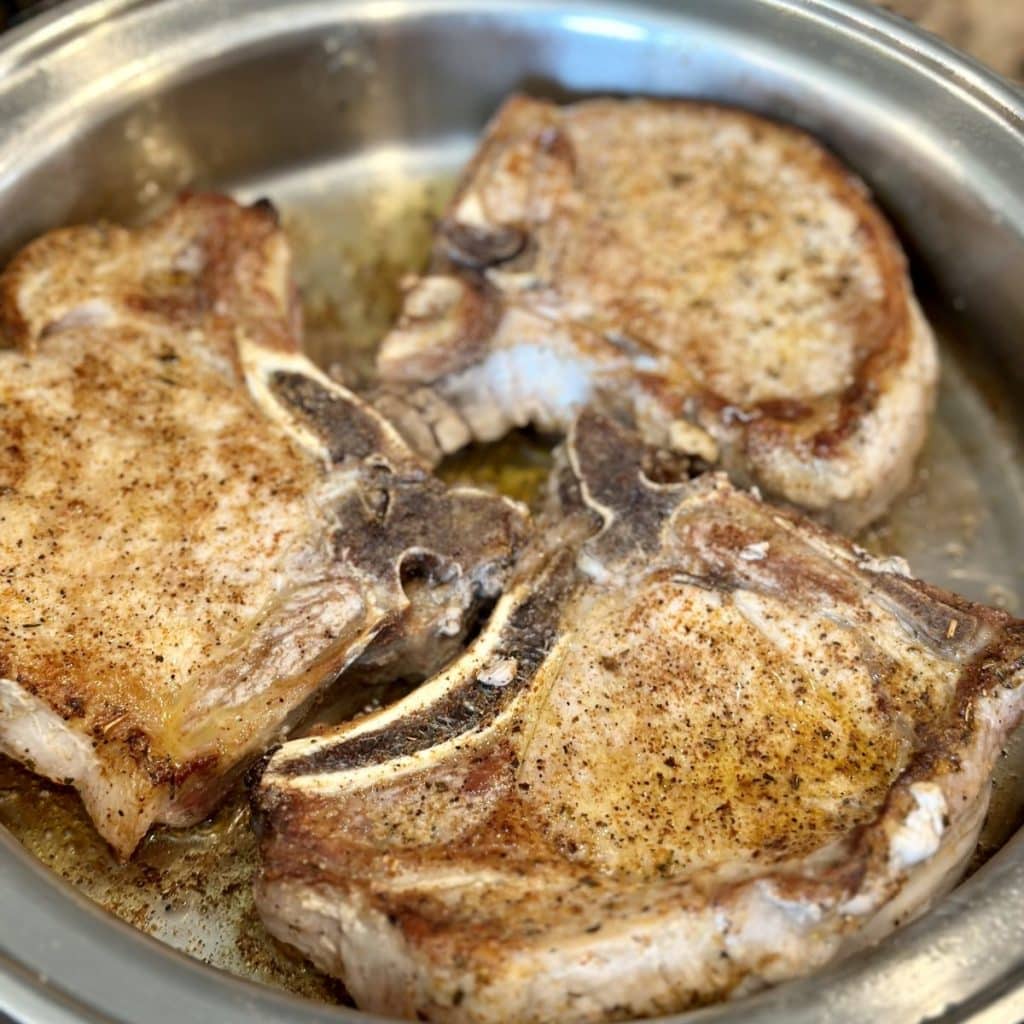 Seasoned pork chops being seared in a skillet.