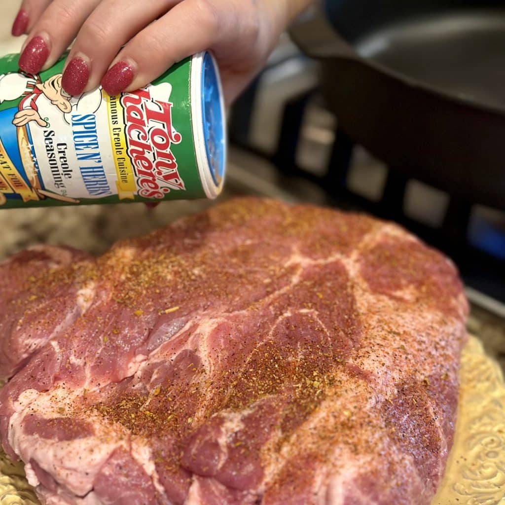 Seasoning a pork butt with cajun seasoning.