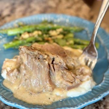 A plate topped with mashed potatoes, pork, gravy and asparagus.