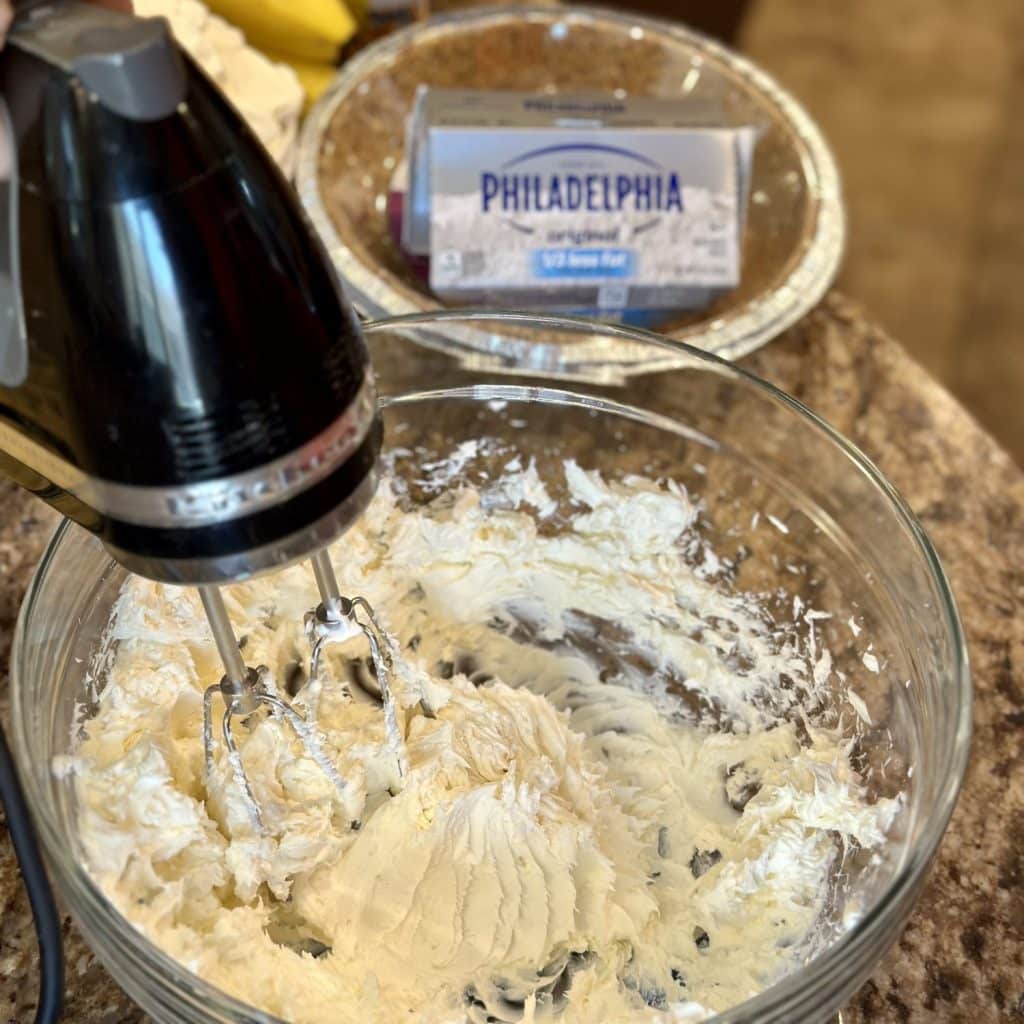Mixer smoothing cream cheese in a bowl.
