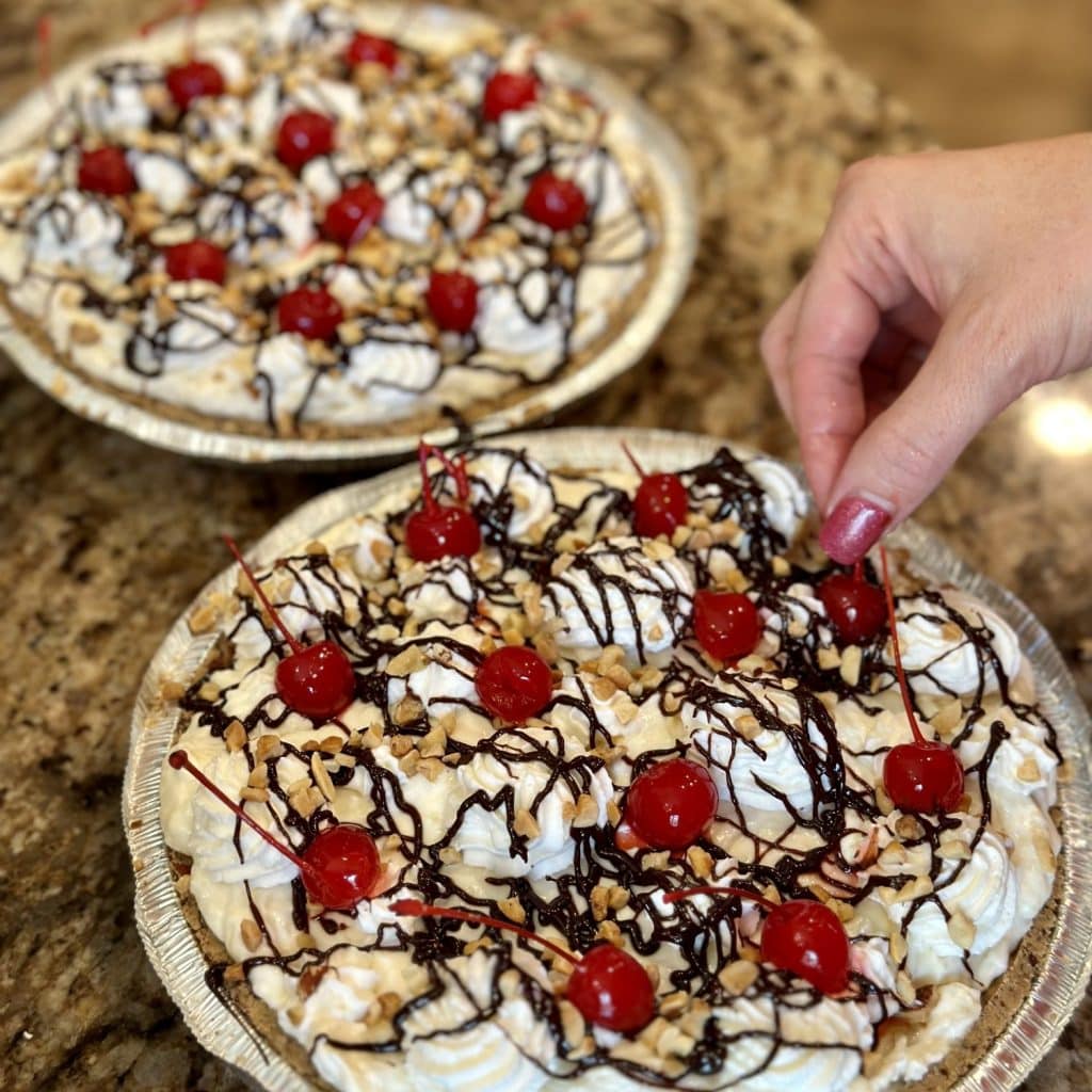 A pie being garnished with chocolate, cherries and sprinkles.
