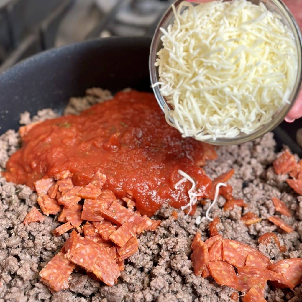Pepperoni, marinara sauce and italian seasoning being added to ground beef in a skillet.