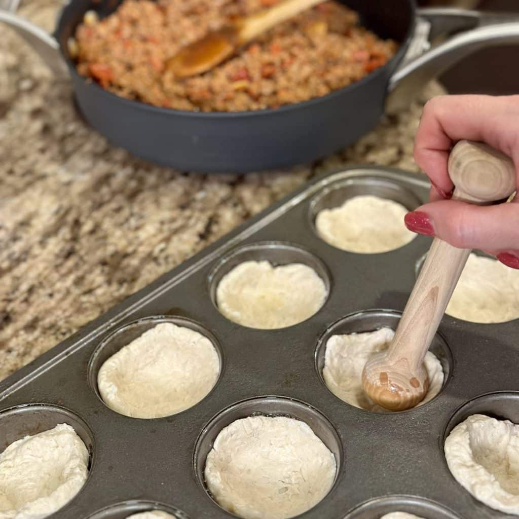 Tampering biscuit dough in a 12-cup muffin pan.