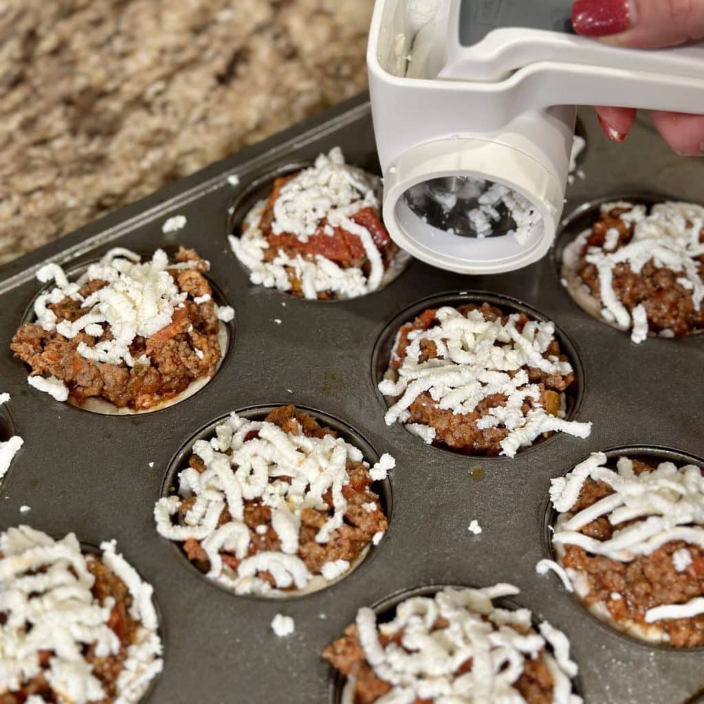 Topping pizza cups with shredded cheese.