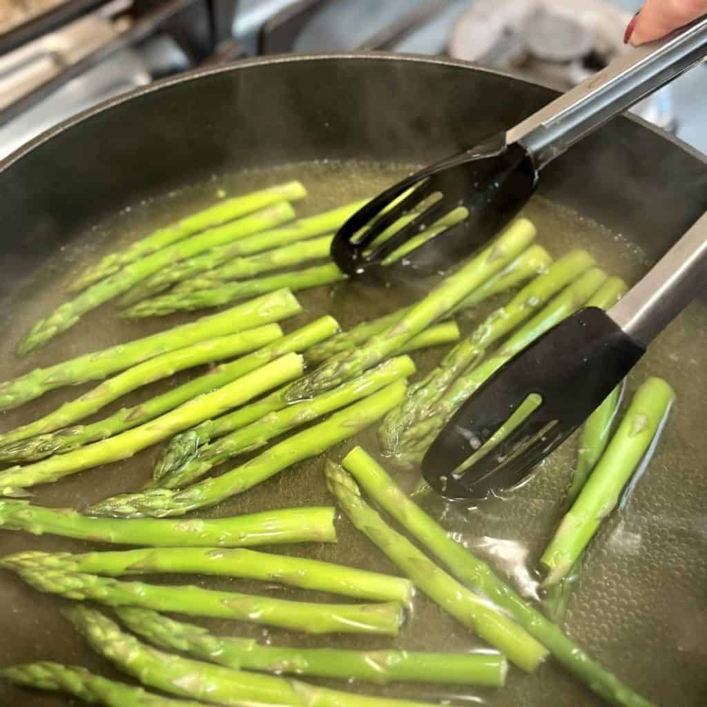 A large skillet with asparagus being boiled inside in water.