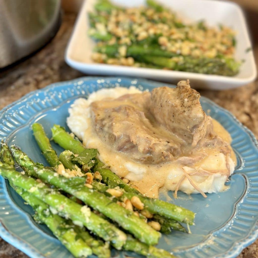 A plate topped with gremolata asparagus, mashed potatoes and pork roast.