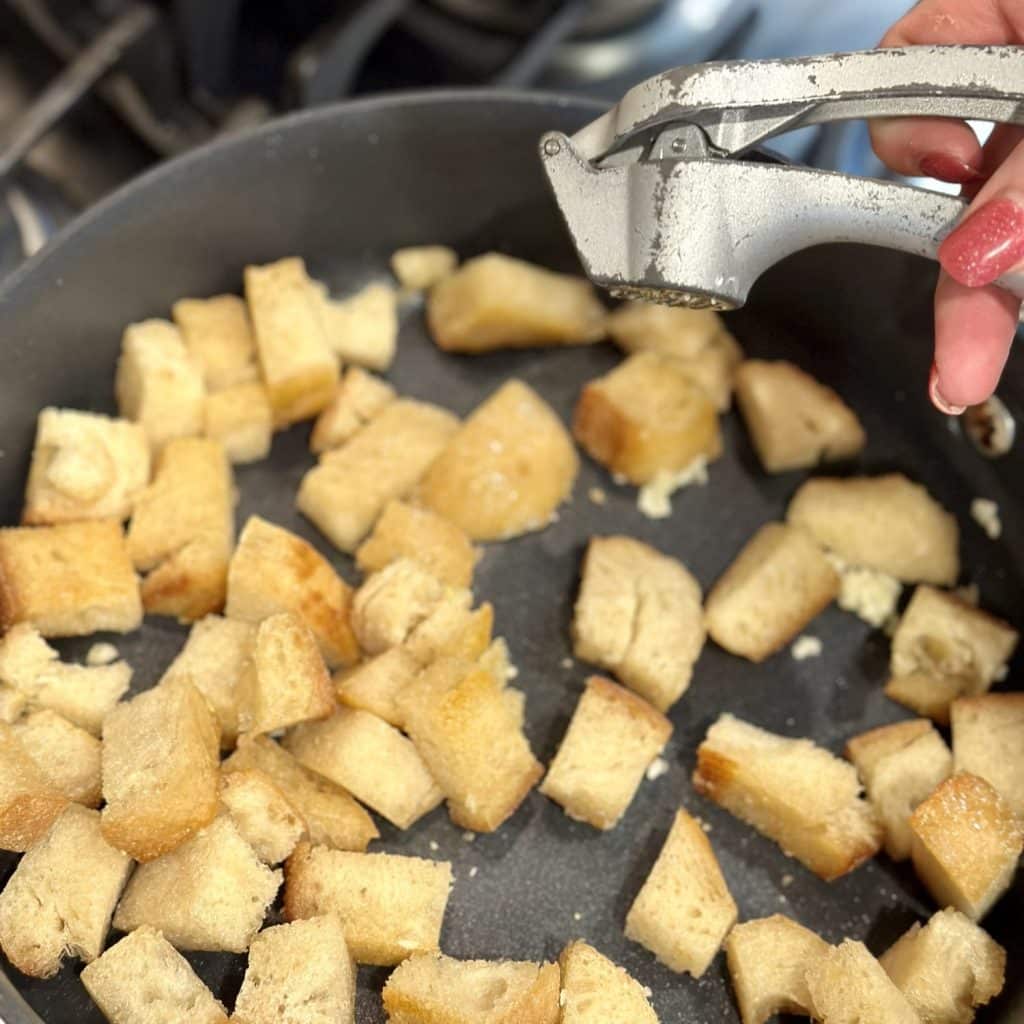 Bread cubes in a large skillet being toasted with fresh garlic.